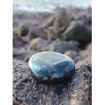 Galet de labradorite irisé bleu posé sur rocher sombre au bord de mer en Bretagne, pierre naturelle associée à l’ancrage, à la clarté d’esprit et à la protection subtile.
