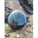 Galet de labradorite aux reflets bleus posé sur rochers et sable en Bretagne, pierre naturelle associée à la stabilité, à la protection douce et à la présence à soi.
