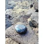 Galet de labradorite aux reflets bleus posé sur rochers bretons près de l’eau, pierre naturelle liée à la tranquillité, au discernement et à l’enracinement intérieur.
