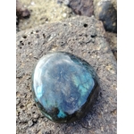 Galet de labradorite aux éclats bleu-vert posé sur roche granitique en bord de mer breton, pierre naturelle associée à la présence à soi, à la lucidité et à l’harmonie intérieure.