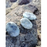 Trois galets de labradorite grise aux reflets bleus posés sur rochers bretons, pierres naturelles associées au calme du mental, à la présence à soi et à la protection douce.