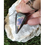 Pendule en labradorite arc-en-ciel tenu entre les doigts, posé sur un amas de quartz blanc et mousse verte, pour se recentrer, se protéger et écouter son intuition.