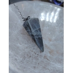 Pendule en labradorite sur chaîne argentée, posé sur une plaque de sélénite blanche, reflets doux, pour protection, intuition et clarté.
