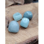 Quatre pierres roulées d’aigue-marine bleu pastel posées sur écorce et bois craquelé, ambiance nature, pour apaiser le mental et faciliter une communication douce. (