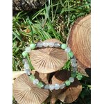 Bracelet endométriose posé sur deux champignons en bois devant feuillage vert, perles vert d’eau et bleutées pour calme intérieur, soutien émotionnel et recentrage