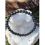 Bracelet hématite 6 mm posé sur bloc de quartz blanc avec écorce et herbes, perles gris acier pour maîtrise de soi, stabilité et contrôle calme