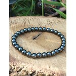 Bracelet hématite 6 mm en cercle sur tranche de bois avec herbes vertes, perles gris foncé métallisé pour volonté ferme, assurance et focus mental