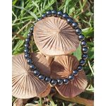Bracelet hématite 6 mm autour de champignons sur herbe verte, perles anthracite brillantes pour aplomb, ancrage et énergie stable