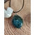 Pendentif en agate mousse poli (forme ronde) sur cordon noir, posé sur un fond en bois avec une petite géode à côté ; pierre associée au chakra cœur, réputée pour apporter apaisement, harmonie émotionnelle et connexion à la nature.