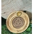 Porte-encens rond en bois motif triquetra, posé sur planche claire avec verdure en fond, ambiance protection, harmonie, rituel.