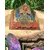 Pyramide orgonite 7 chakras avec fleur de vie et spirale de cuivre, posée sur une tranche de bois en extérieur (herbe, pierre violette au premier plan) ; évoque harmonie, protection, ancrage.