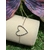 Bracelet chaîne fine en acier inoxydable, pendentif cœur ajouré; posé sur support blanc en extérieur, herbe en fond et papillon violet.