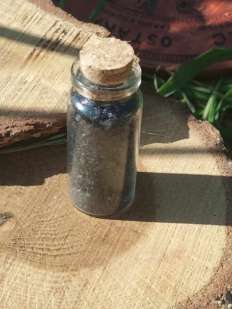 Sel noir ritualisé fait maison en flacon en verre avec bouchon liège, photo sur rondin de bois et décor naturel; usage rituel protection, purification, ancrage, coupure des énergies lourdes et soutien des intentions.