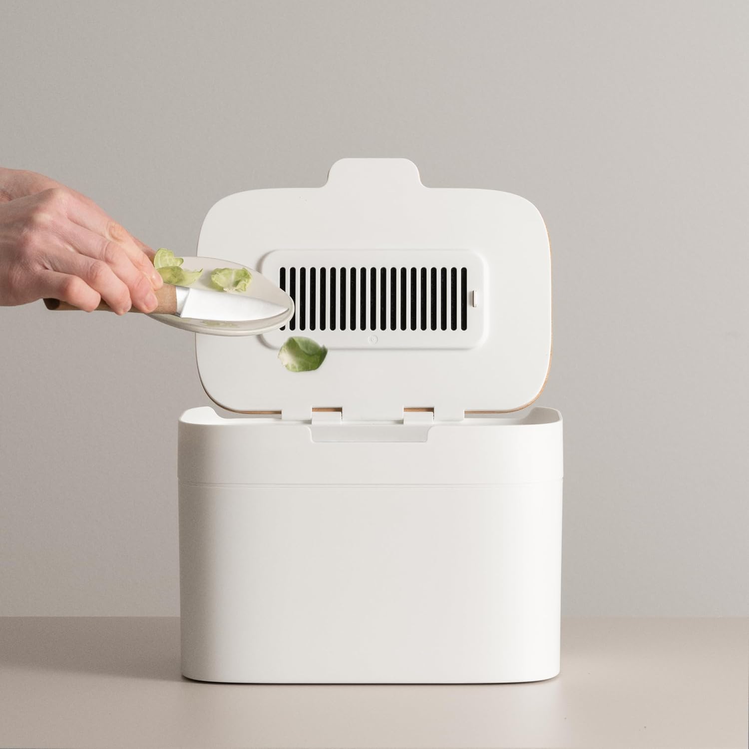 Main déposant des épluchures dans le seau Elin, couvercle ouvert avec sa grille de filtre à charbon