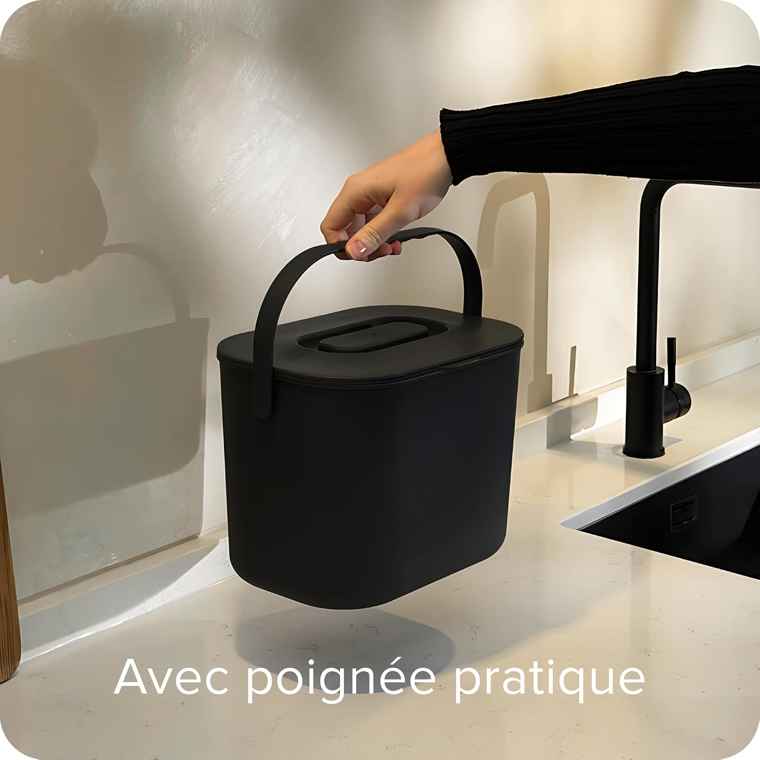 Main portant le seau à compost noir par son anse, au-dessus dun plan de travail