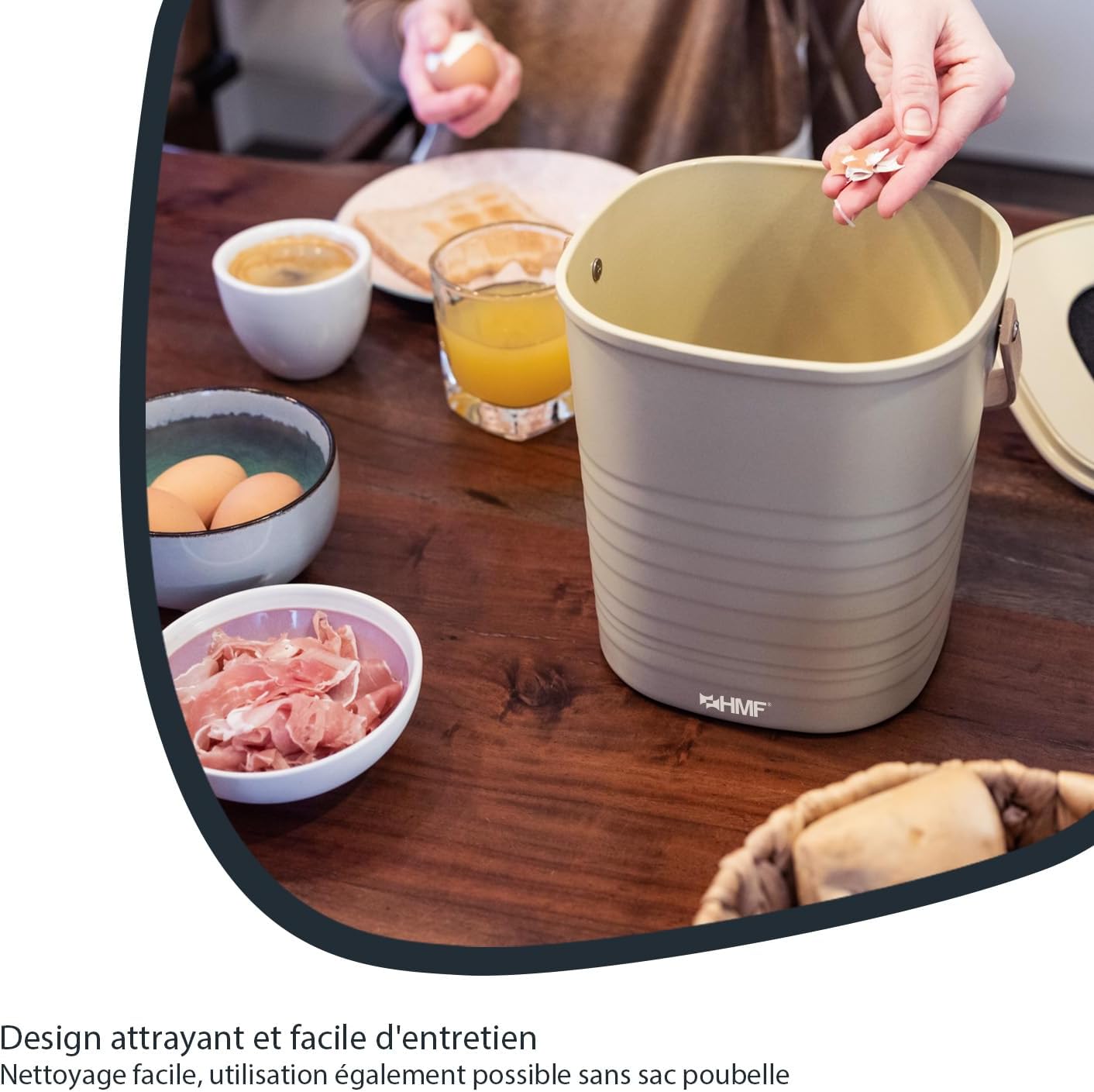 Main jetant des épluchures dans le seau beige sans couvercle, posé sur une table de petit-déjeuner