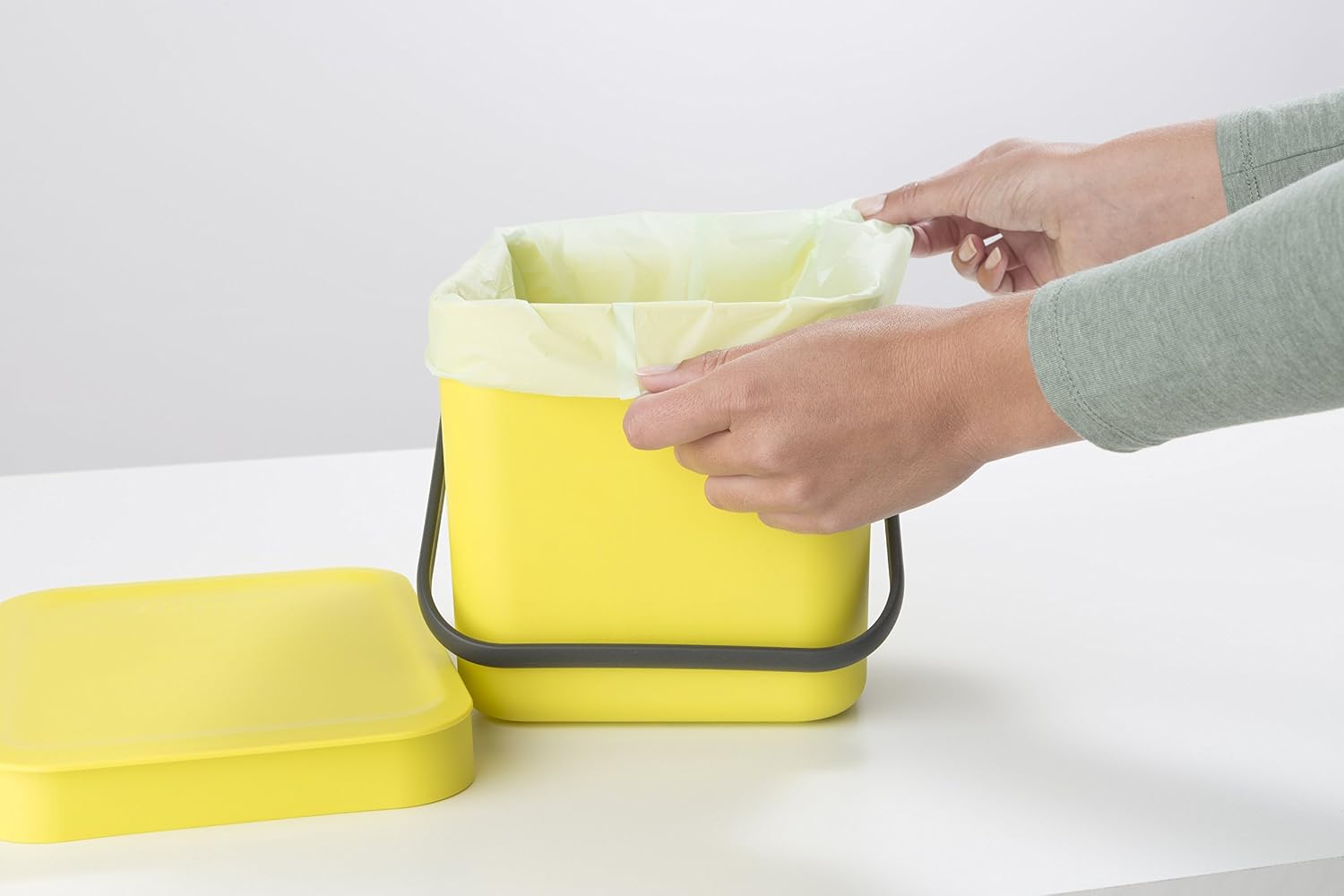 Mains installant un sac compostable clair dans un seau de cuisine jaune à anse