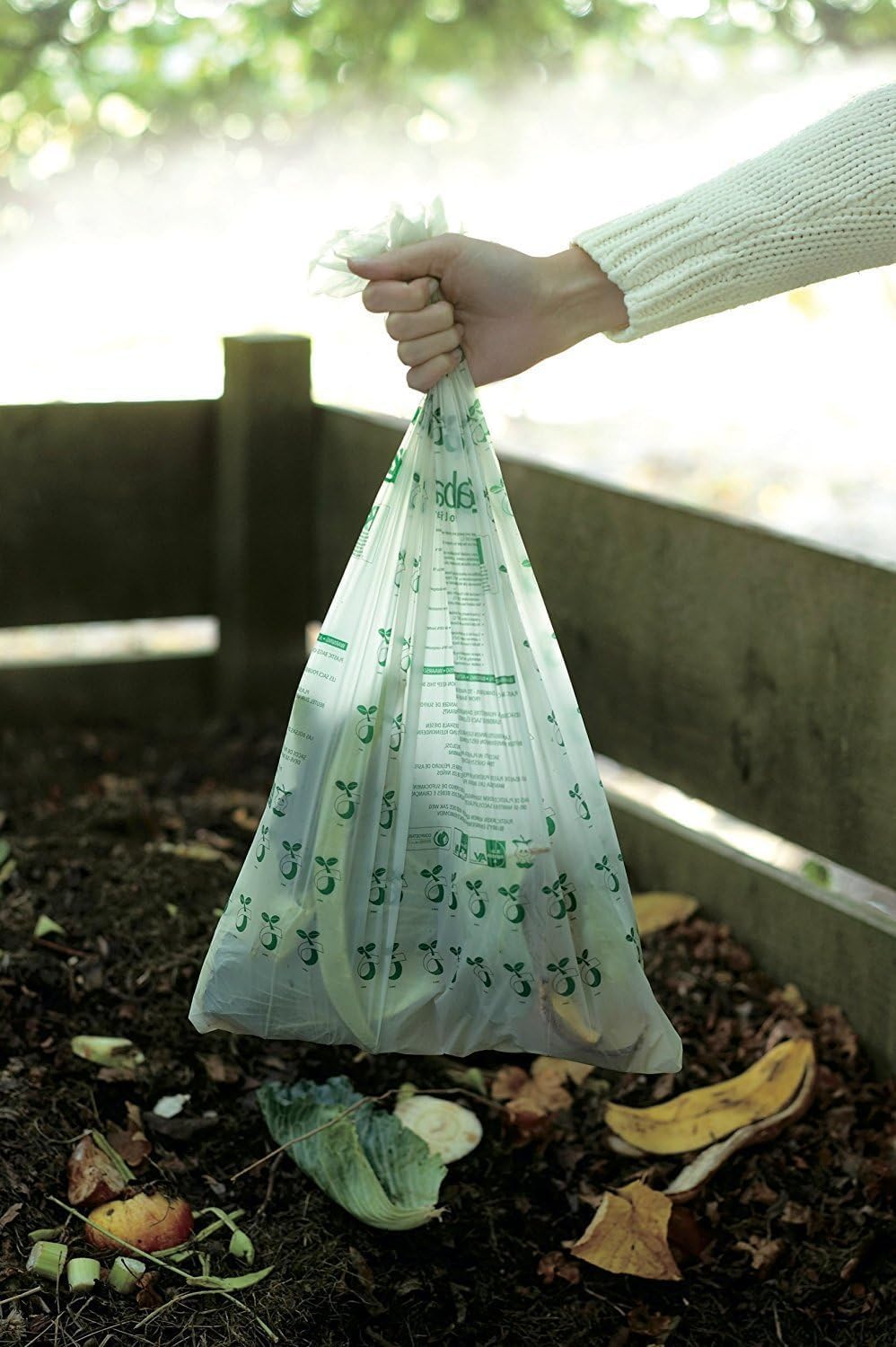 Main tenant un sac compostable rempli dépluchures au-dessus dun bac à compost en bois