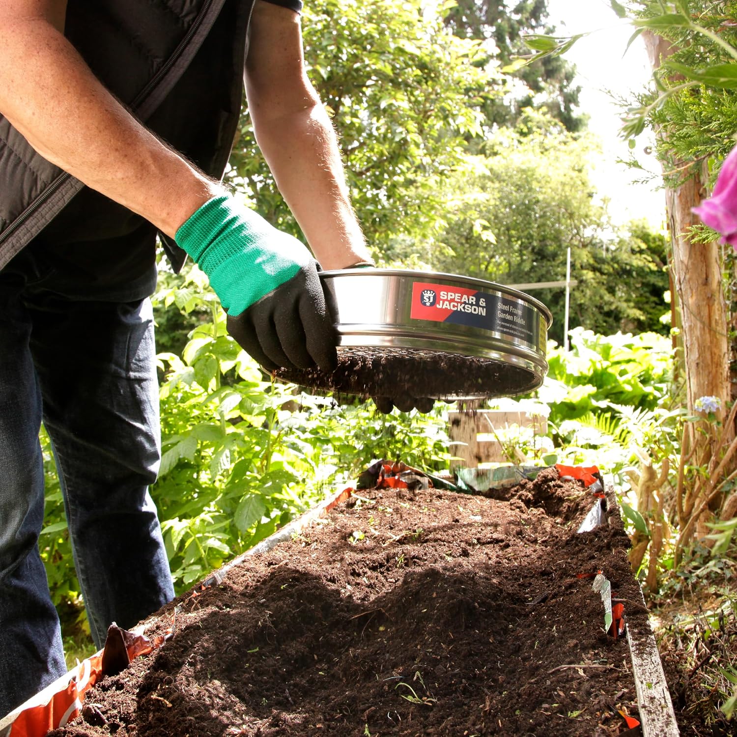 Jardinier ganté tenant le tamis rempli de terre au-dessus dun carré potager