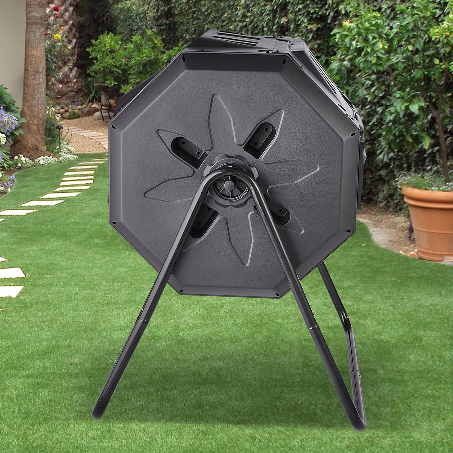 Composteur rotatif noir vu de côté sur son support, dans un jardin
