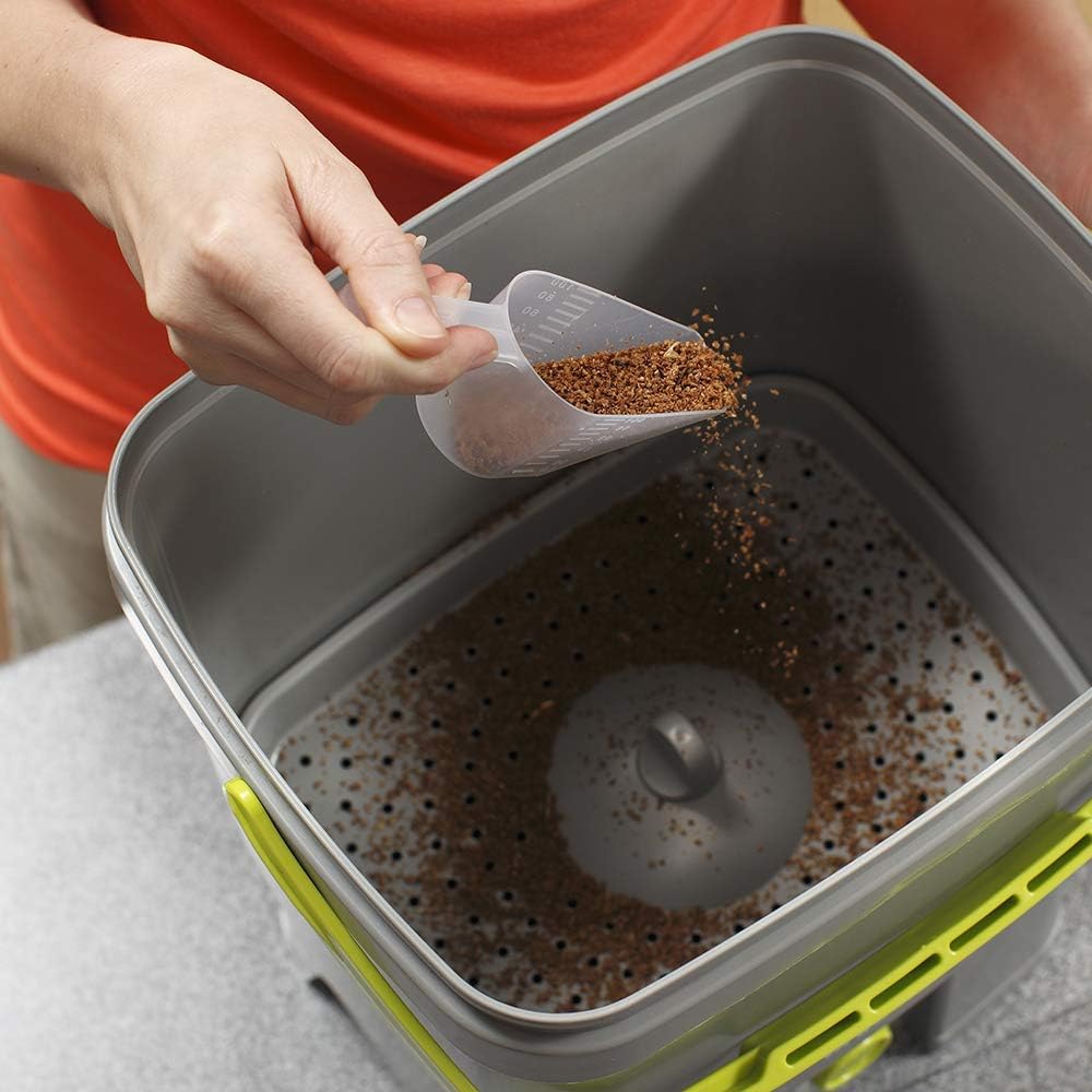 Main versant lactivateur avec la cuillère doseuse au fond dun seau bokashi gris et vert