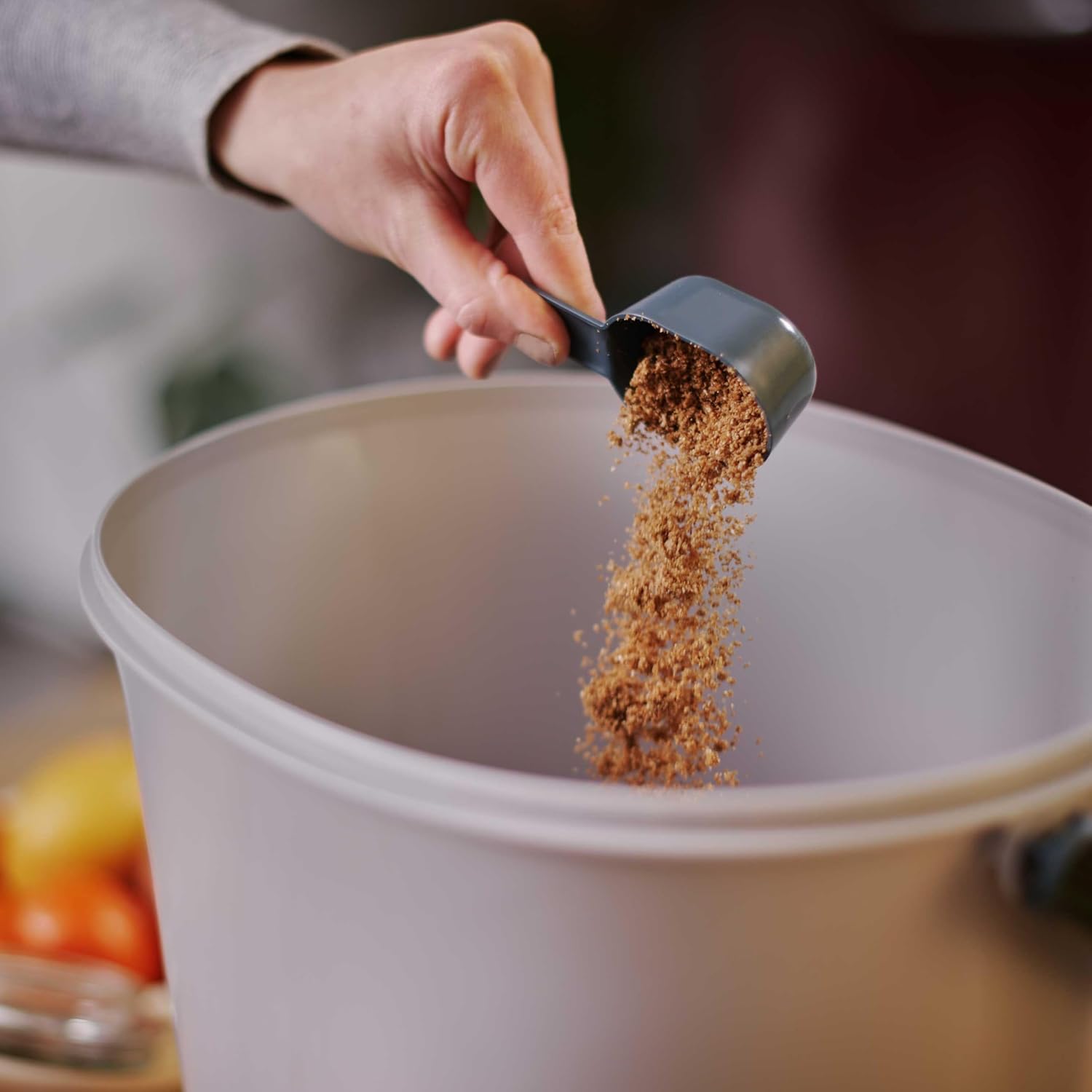 Activateur bokashi versé à la cuillère grise dans un seau clair vide