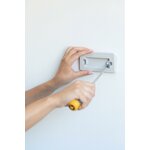 Mains vissant le support mural du bac Curver sur un mur blanc