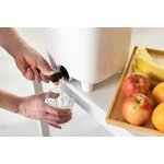 Mains remplissant un verre au robinet du seau bokashi pour recueillir le jus, avec des fruits