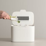 Main déposant des épluchures dans le seau Elin, couvercle ouvert avec sa grille de filtre à charbon