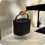 Main portant le seau à compost noir par son anse, au-dessus dun plan de travail