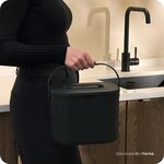 Femme transportant le seau à compost noir dans une cuisine, avec robinet noir
