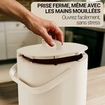 Main ouvrant le couvercle du seau beige dune seule main, près dun plan de travail
