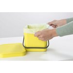 Mains installant un sac compostable clair dans un seau de cuisine jaune à anse
