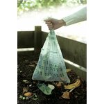 Main tenant un sac compostable rempli dépluchures au-dessus dun bac à compost en bois