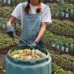 Jardinière en salopette retournant les épluchures dun composteur bleu avec laérateur