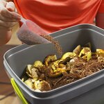 Activateur saupoudré à la cuillère sur des épluchures dans un seau bokashi