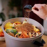 Couche dactivateur bokashi saupoudrée sur des épluchures de légumes et dagrumes dans un seau