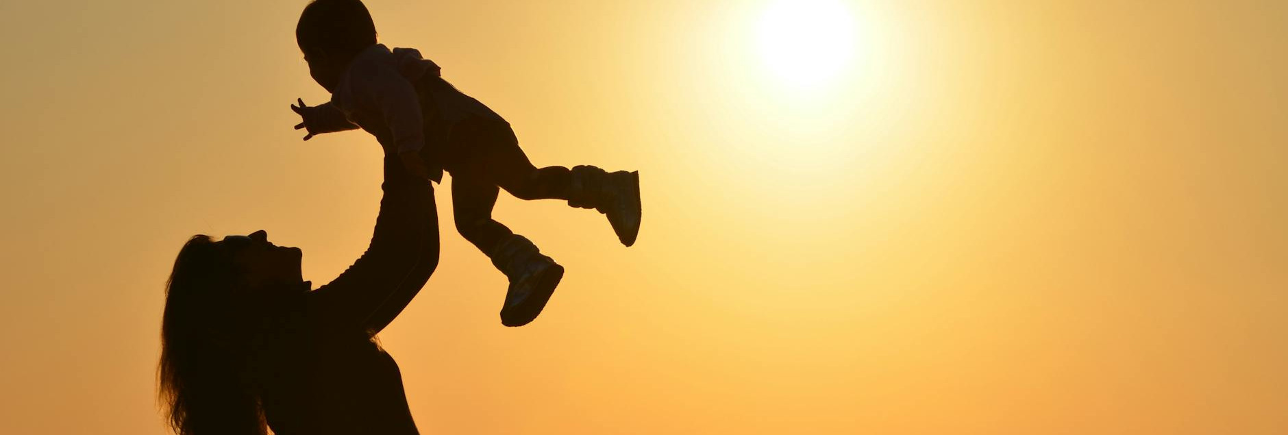 silhouette of a mother lifting her child at a sunset beach capturing warmth and love