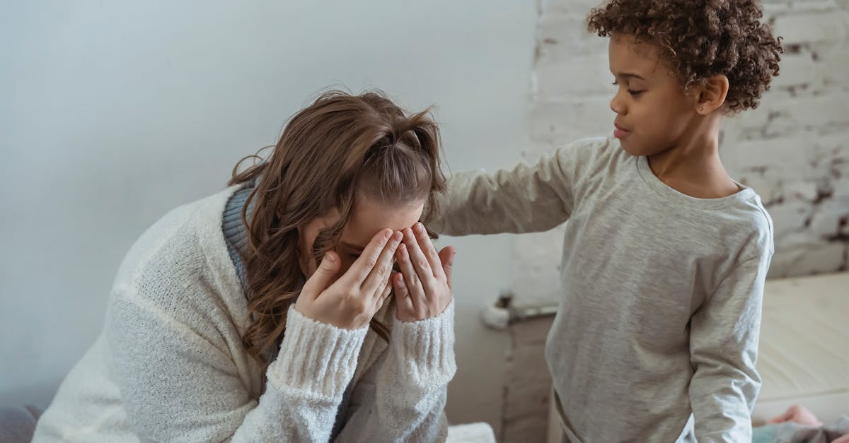 caring african american son touching shoulder of upset faceless mother covering face while sitting in light room near wall at home
