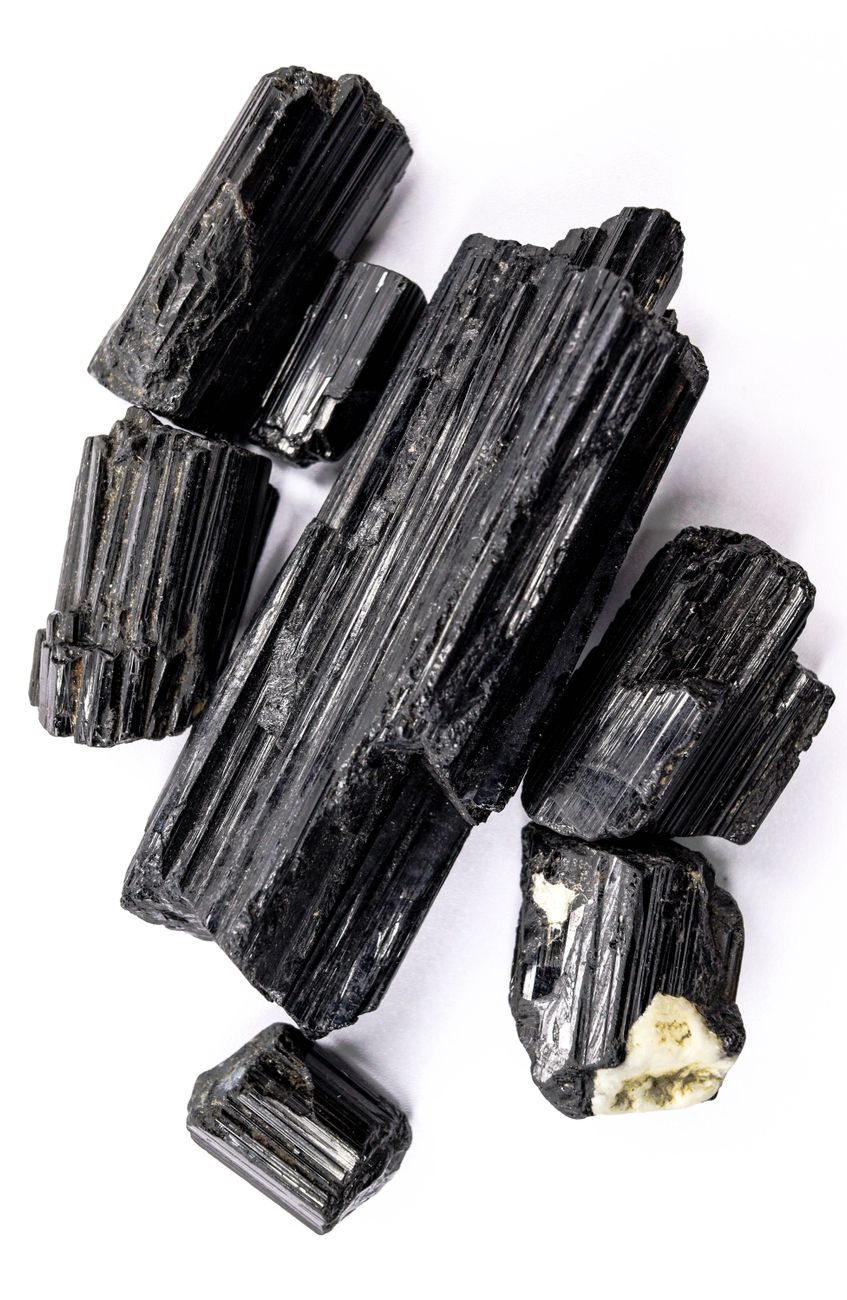 Cristaux de tourmaline noire disposés sur une surface blanche immaculée, mettant en valeur leur texture et leur éclat naturels