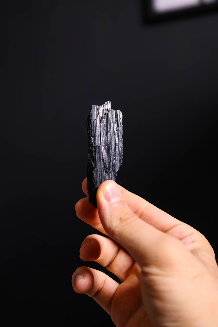 Gros plan dun minéral de tourmaline noire tenu par une main sur un fond sombre
