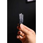 Gros plan dun minéral de tourmaline noire tenu par une main sur un fond sombre
