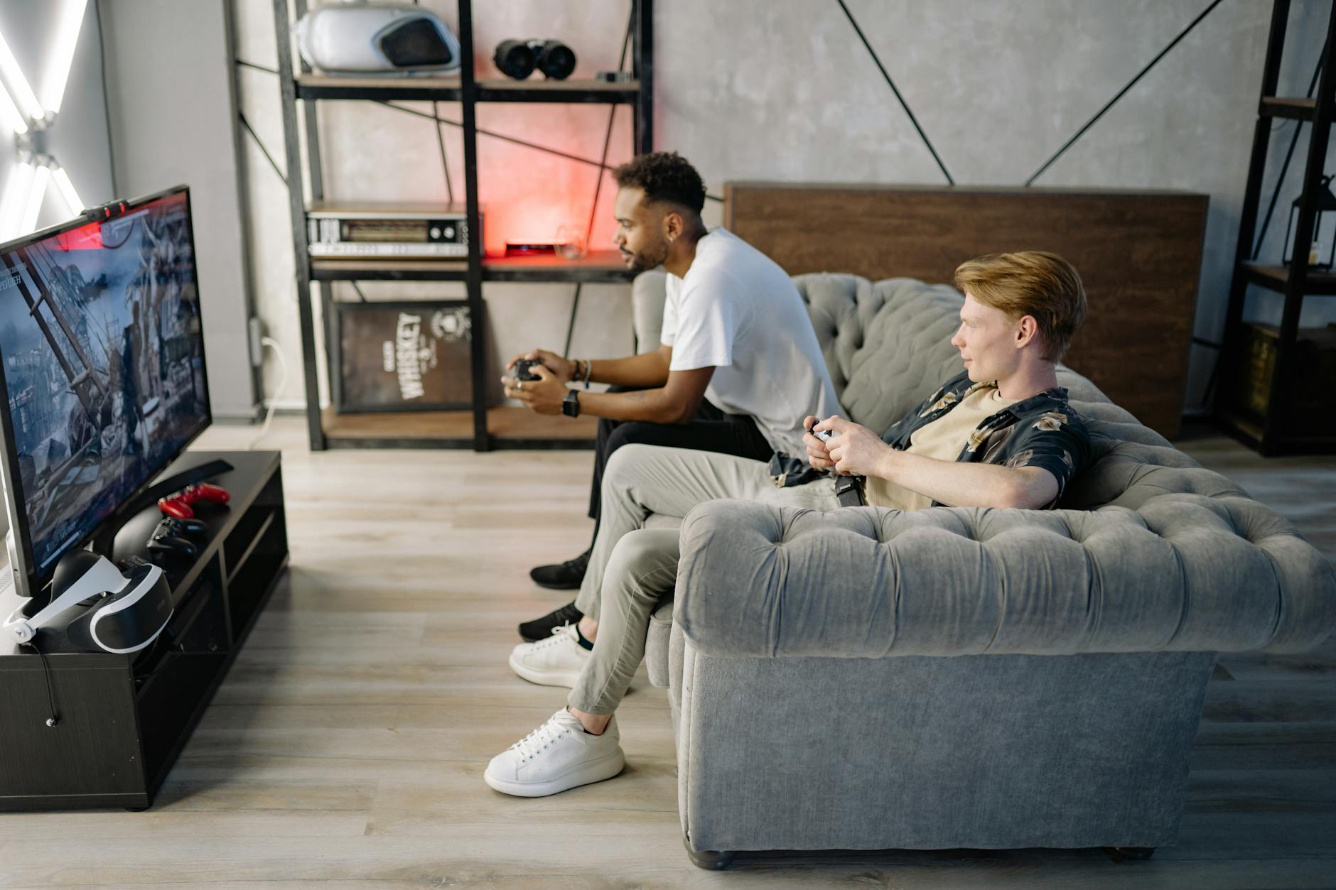 two adult men playing video games on a couch enjoying leisure time indoors
