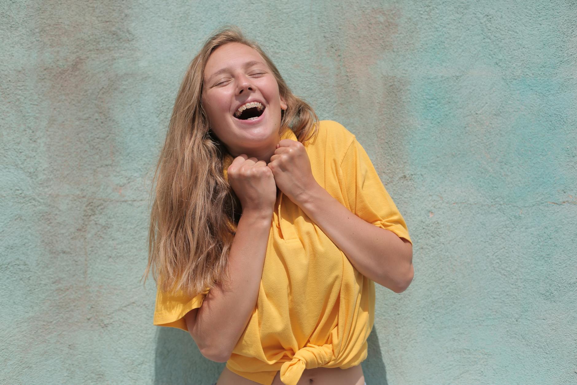 a cheerful woman in a yellow top laughing joyfully against a pastel colored wall