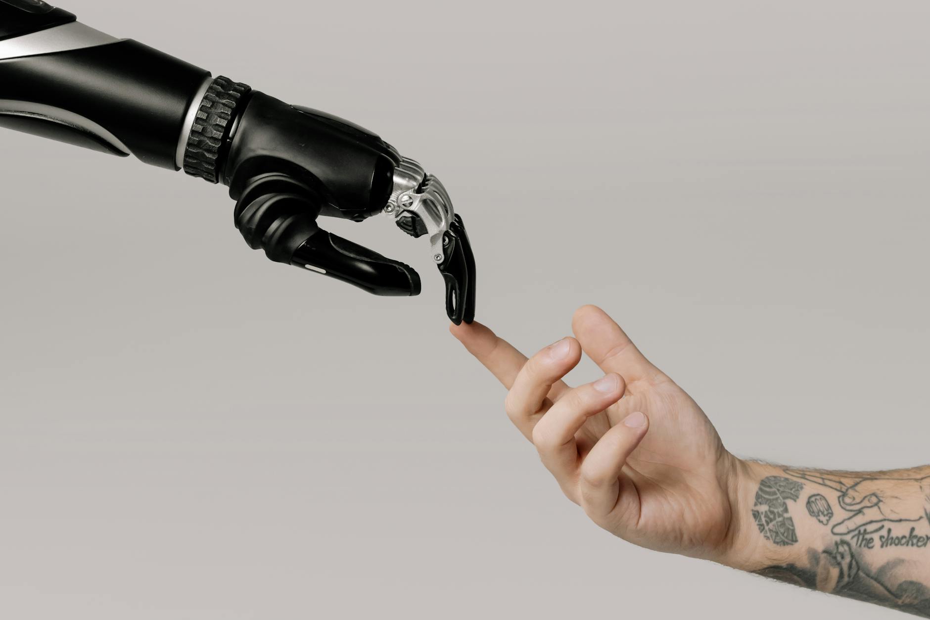 a human hand with tattoos reaching out to a robotic hand on a white background