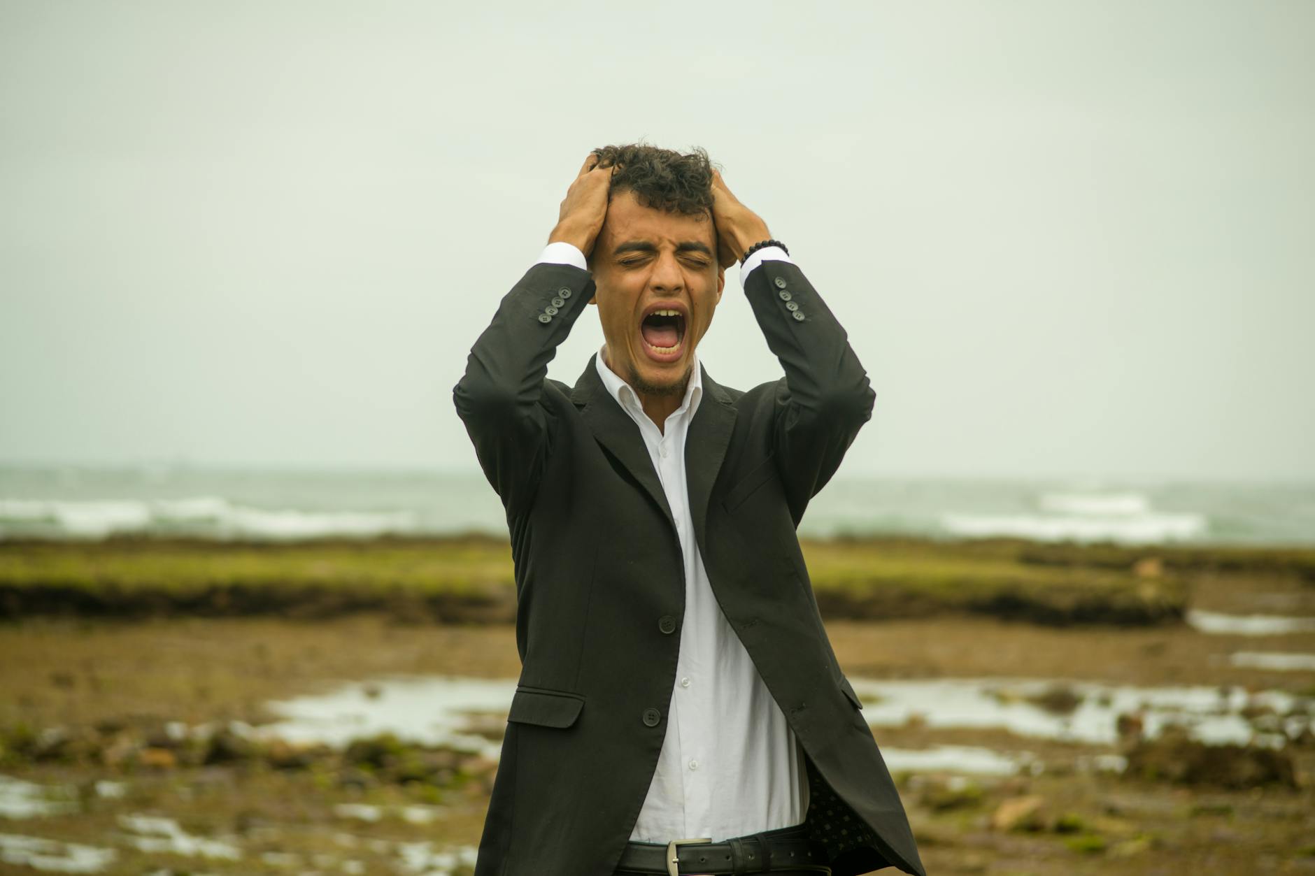 a man in a suit screams in frustration while standing on a windy beach emotional stress concept