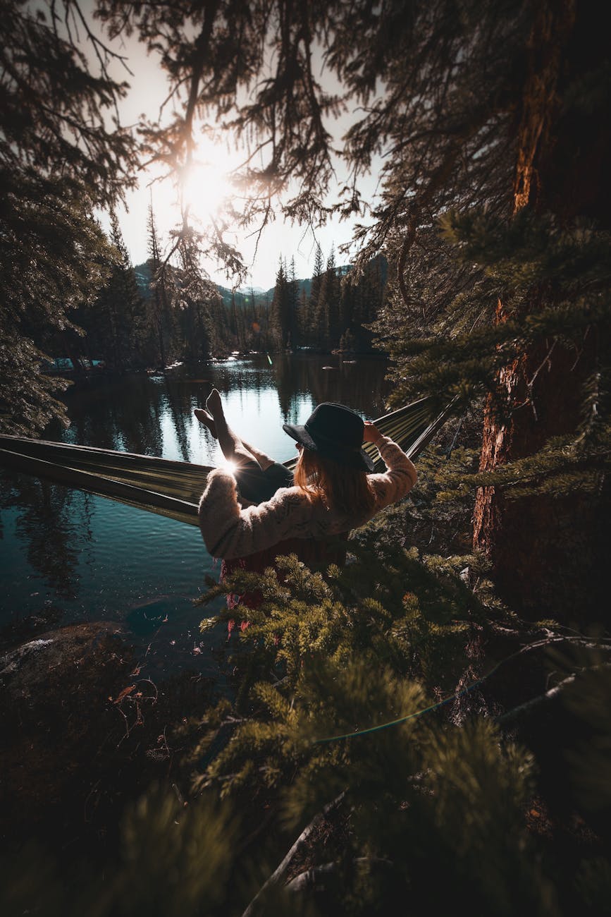 a woman enjoys a peaceful moment in a hammock by a serene lake surrounded by trees during sunset