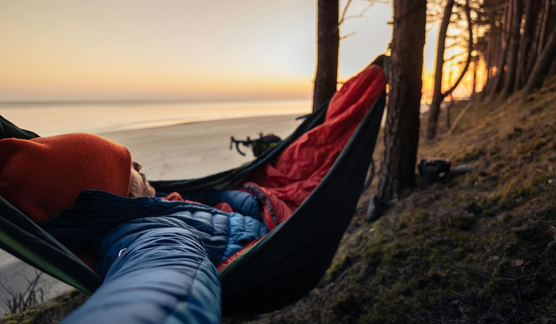 person sleeping in hammock on forested beach at sunset enjoying outdoor leisure