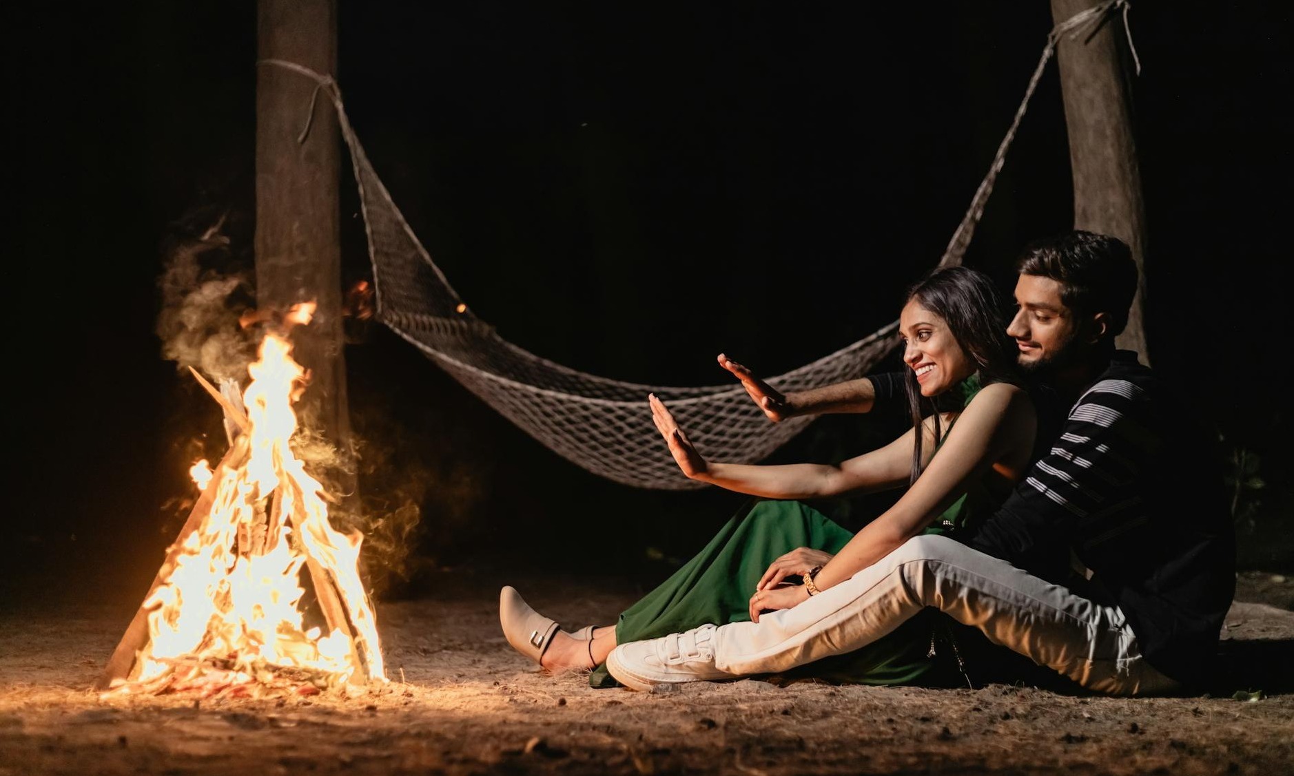 a couple enjoying a warm campfire night embracing under a hammock in an outdoor setting