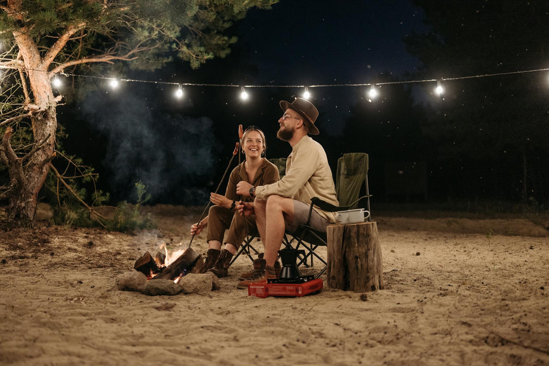 happy couple sitting by a campfire roasting sausages and enjoying the night outdoors